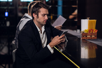 beautiful young guy surfing the Internet in a smartphone behind the bar in a nightclub.