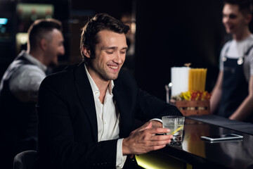 portrait of a young man in a shirt and jacket at the bar with a cocktail in his hands.