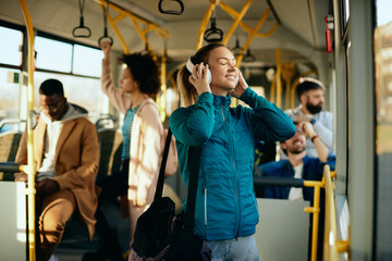 Happy athletic woman listening music with eyes closed while traveling by bus.