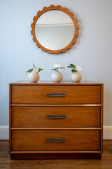 Mid-century modern dresser with trio of white vases and round mirror.