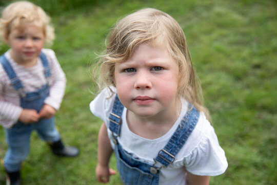 Portrait serious blonde girl in overalls with sister