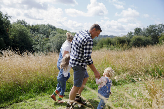 Family holding hands walking in sunny rural summer field