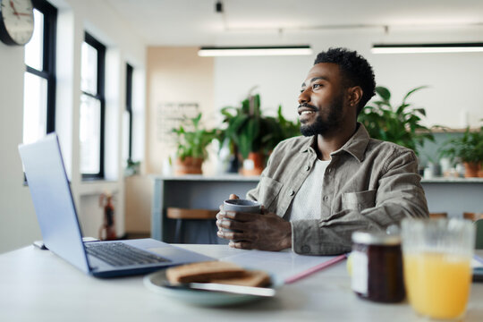 Thoughtful businessman with coffee working at laptop in office