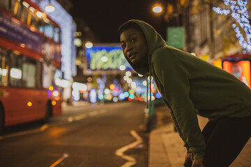 Young female jogger waiting to cross city street at night, London, UK