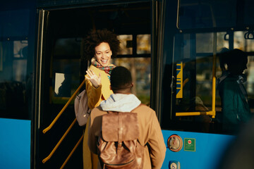 Happy African American woman waving to her boyfriend while getting in a bus.