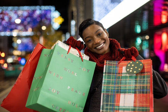 Portrait happy young woman Christmas shopping in city at night
