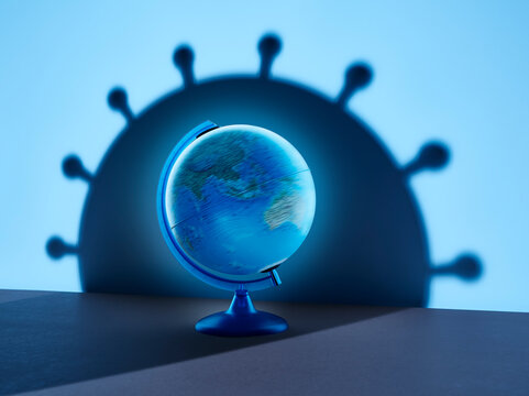 Spinning globe casting large blue coronavirus bacterium shadow