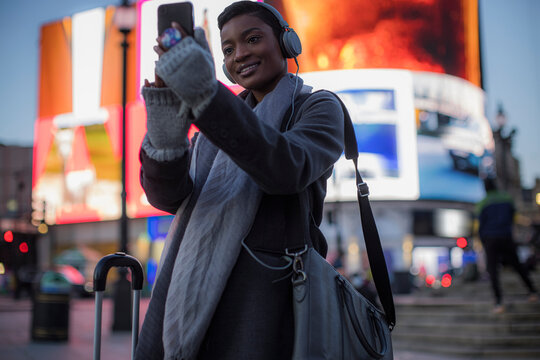 Young woman taking selfie on city street at night, London, UK