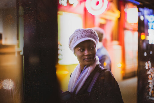 Young woman in hat looking over shoulder at bus stop at night