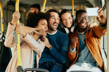 Cheerful friends taking selfie with smart phone while commuting by bus. © Drazen