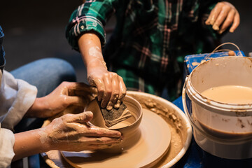 close-up of the hands of a potter's girl and a child who are sculpting clay dishes on a potter's wheel