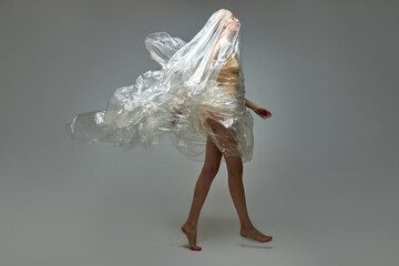 portrait of caucasian short-haired woman wrapped in plastic bags, polyethylene. posing at camera isolated over gray background