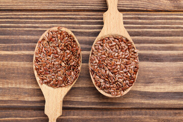 Flax seeds in spoons on brown wooden background