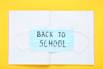 Inscription Back to School on medicine mask with notepad on yellow background