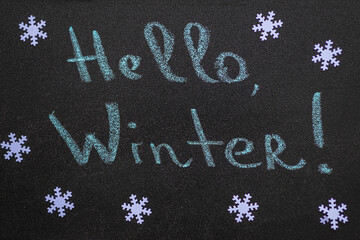 Fototapeta na wymiar New year and Christmas concept. White snowflakes and handwritten inscription Hello Winter. Chalk inscription on black chalkboard.