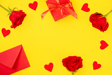 Valentine's Day. Frame made of red flowers, a gift on a yellow background. Valentine's day background. Flat lay, top view, copy space.