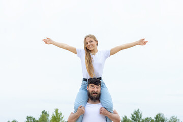 Obraz premium Happy people! Man holds on his shoulders a young woman while keeping arms outstretched, on outdoors.