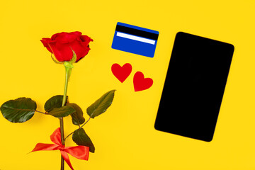 Valentine day internet sales concept, internet shopping holiday background. Tablet screen with copy space lay on yellow background with pink flower and credit card, top view.