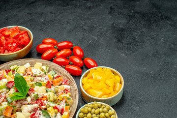 side close view of bowl of vegetable salad with veggies on side and place for your text on dark grey background
