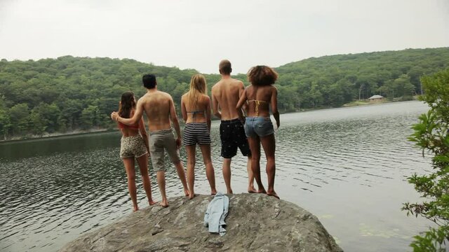 Friends standing on rock at lake throwing hands in air