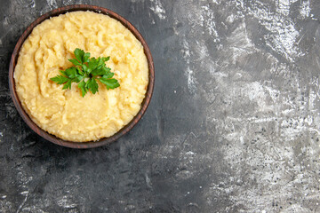 top view mashed potatoes in wooden bowl decorated with parsley herbs on dark background with copy space