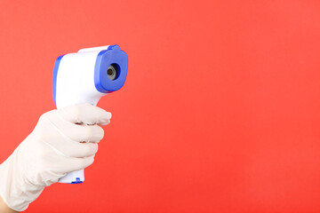 Medical infrared thermometer in doctor hand on red background