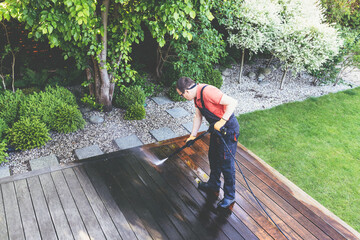 power washing - worker cleaning terrace with a power washer - high water pressure cleaner on wooden terrace surface