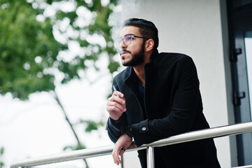 Middle eastern entrepreneur wear black coat and blue shirt, eyeglasses against office building...