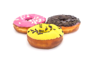 three traditional American donuts with chocolate, yellow, pink icing and sprinkles on a white
