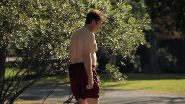 Tracking shot of shirtless man reading morning newspaper outdoors