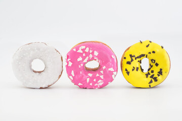 three traditional American donuts with pink, yellow, white icing and sprinkles isolated on a white