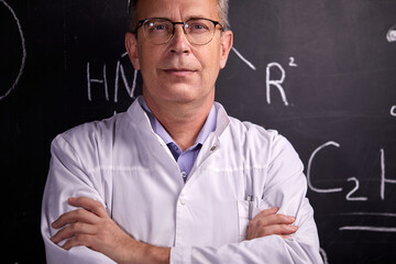 portrait of pleasant intelligent male professor in university, posing near blackboard with formulas. science, chemistry concept
