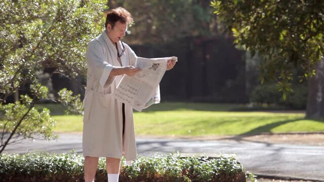 Man wearing bathrobe reading morning newspaper outdoors