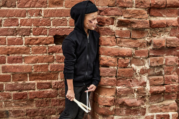 street boy is having fun, playing with slingshot, wearing dirty clothes, enjoy life despite social...