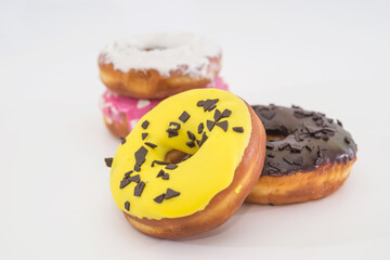  traditional American donuts with chocolate, pink, yellow, white icing and sprinkles on a white plate.