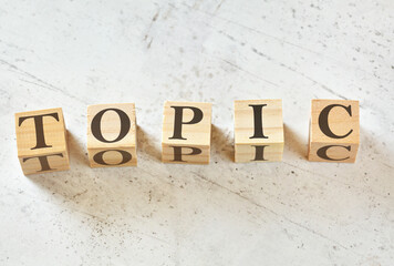 Five wooden cubes with word TOPIC on white stone like board, view from above
