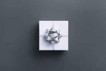 White square gift box with silver bow on gray background. Top view.