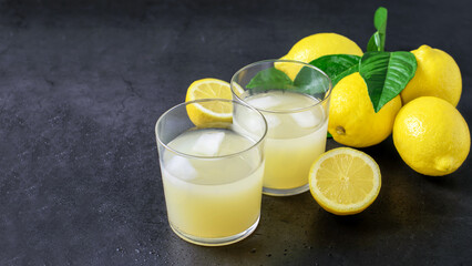 Two glasses with lemon fresh and ripe lemon fruits on the gray background close up, side view.