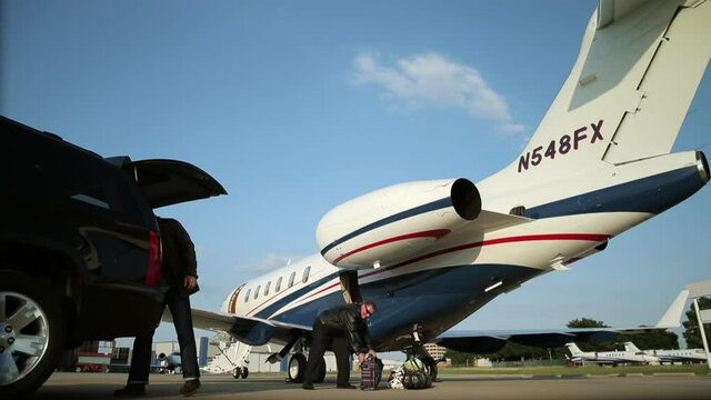 Caucasian man passing luggage to pilot near private jet