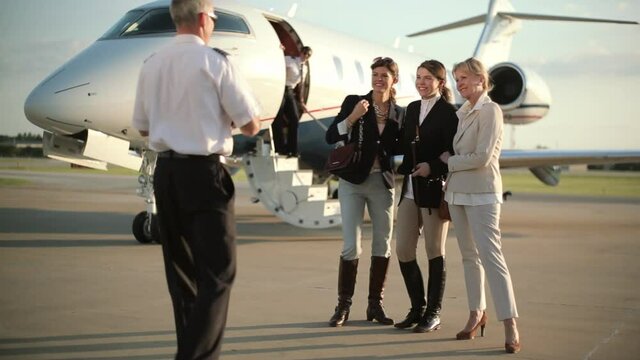 Caucasian pilot photographing women on tarmac near private jet