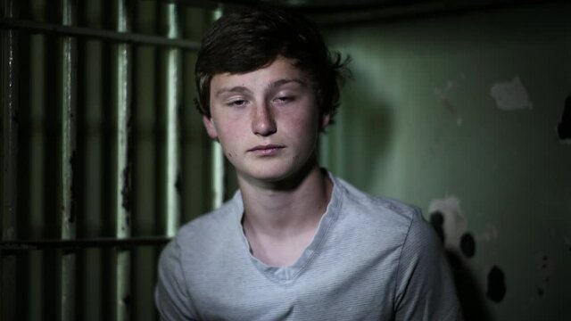 Close up of Caucasian teenage boy in dark jail cell