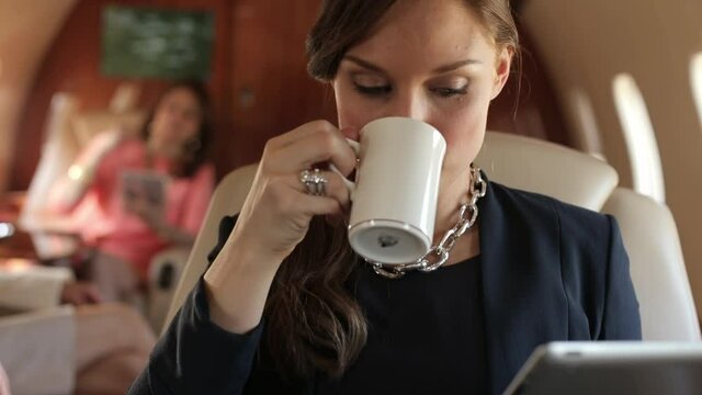 Businesswoman drinking coffee and reading digital tablet on private jet
