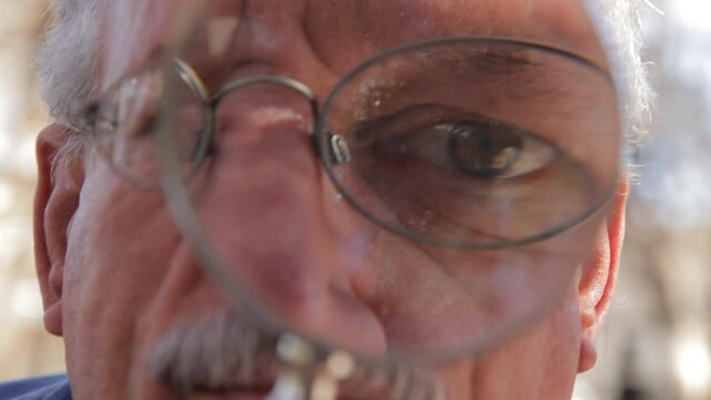 Older man holding magnifying glass in front of face