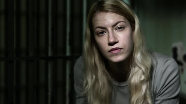 Caucasian woman sitting in dark jail cell looking at camera