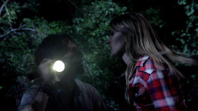 Close up of couple cowering in fear in woods at night