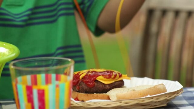 Close up of Caucasian boy dousing cheeseburger with mustard and ketchup