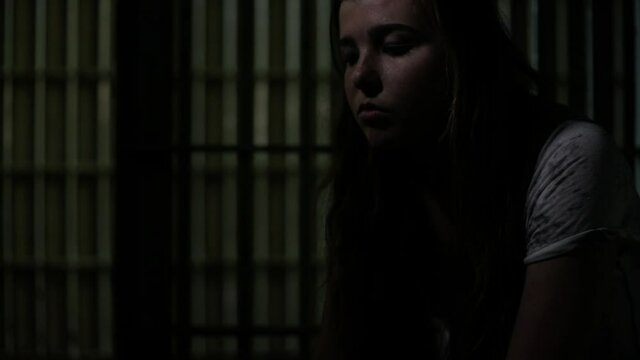 Caucasian teenage girl sitting in dark jail cell