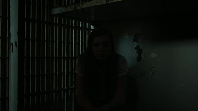 Caucasian teenage girl sitting in dark jail cell