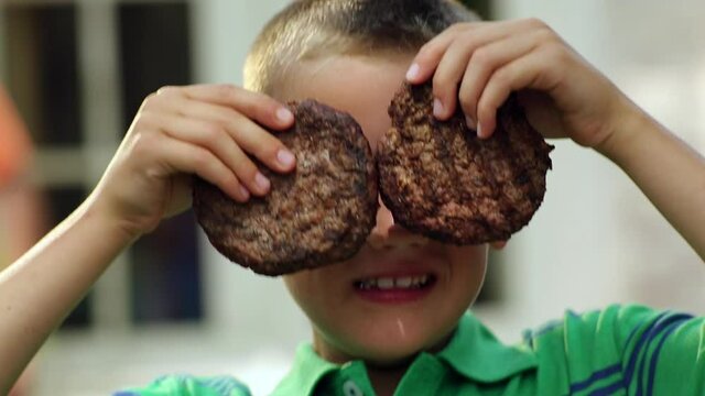 Close up of Caucasian boy holding hamburger patties over eyes