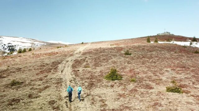 A drone capture of a couple with big backpacks hiking to Seiner Kreuz, a peak in Austrian Alps. Cross on the peak. There are a few snow fields around. Early spring in the mountains. Wanderlust
